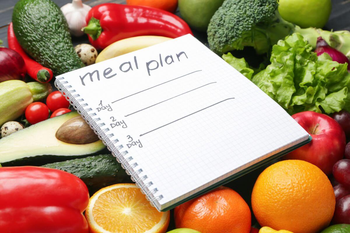 The image shows fruits, vegetables, and a notebook with notes referring to meal plans to reduce food waste making it a smart way to save money.