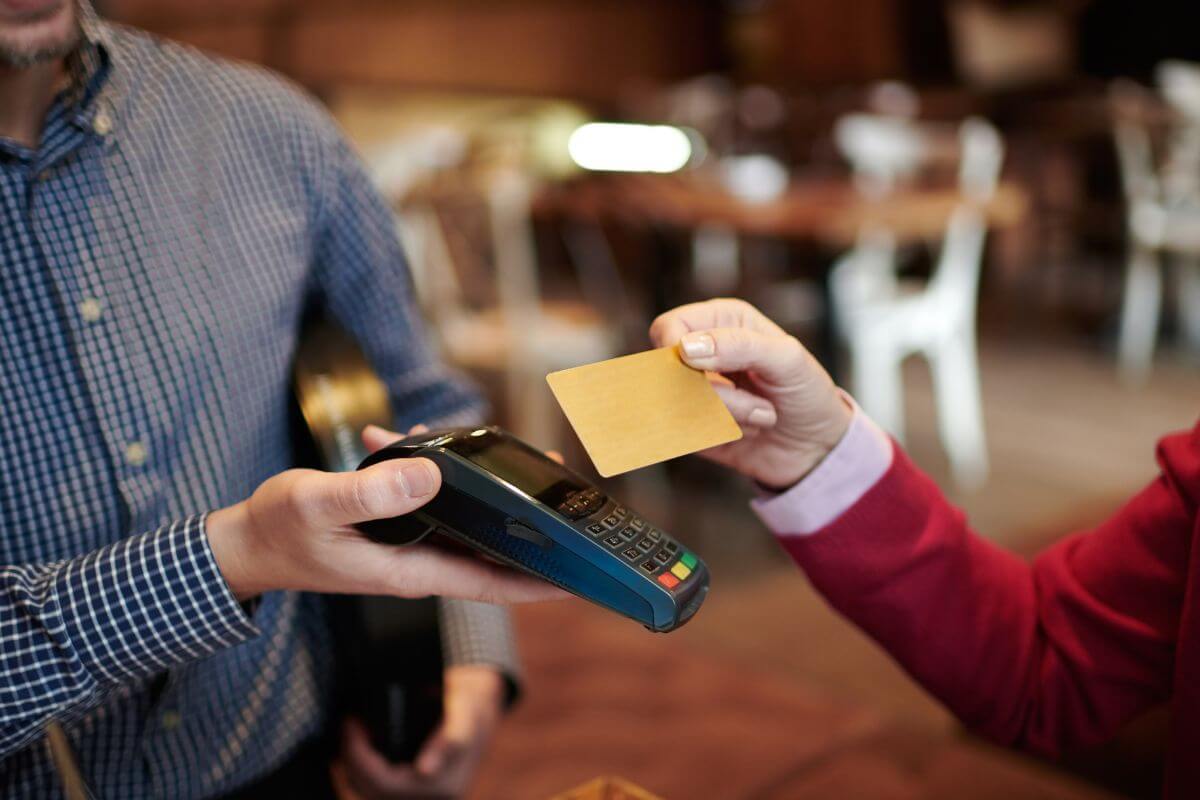 The photo shows a waiter holding a card machine swiper and a customer's hand tapping the card to it which means limiting credit card use and reserving for emergencies and avoiding unnecessary debt.