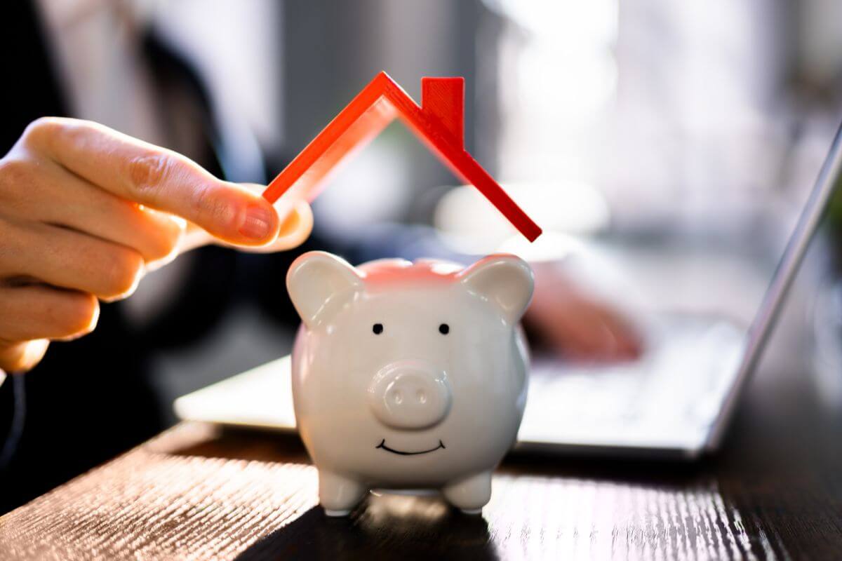 The picture shows a girl using a laptop and holding a house roof figure placed at the top of a piggy bank indicating to find more ways to save money fast and build a better financial future.