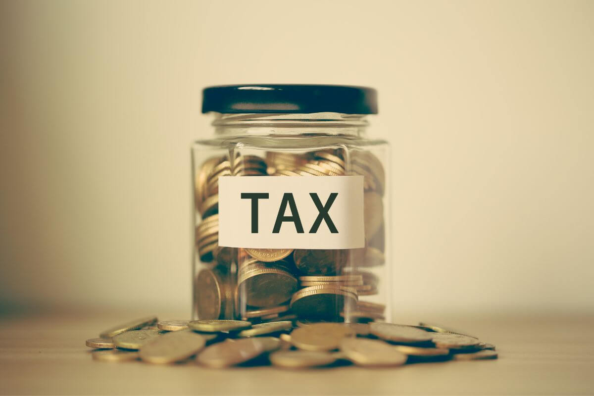 The picture of coins on the table and a jar filled with coins and with a note referring to prioritizing tax-efficient investment strategies to optimize your wealth preservation.