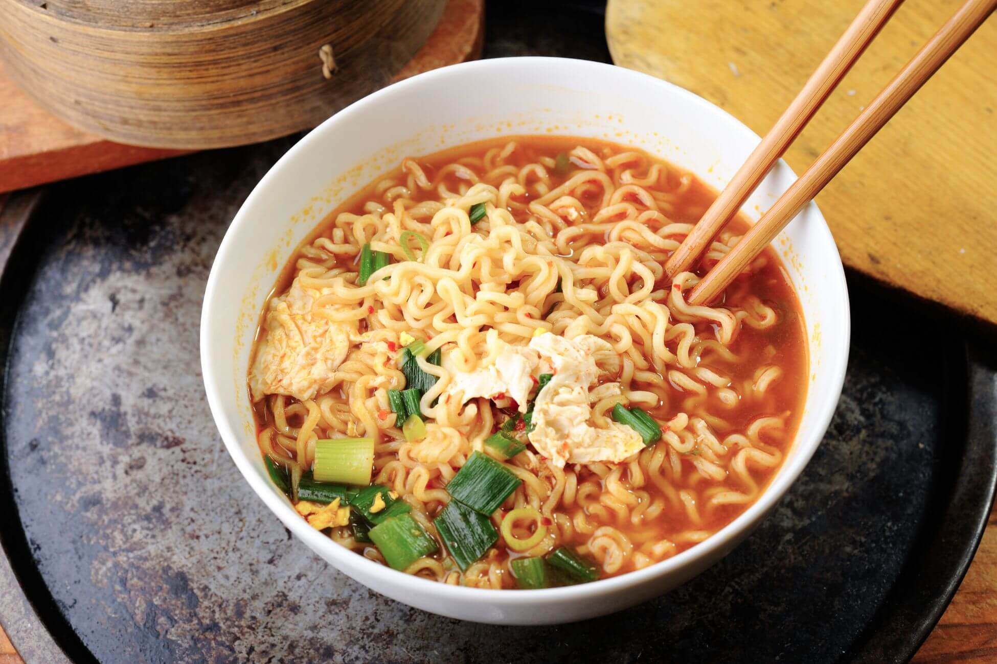 The photo tells about a ramen noodles inside a bowl with egg and spring onion and a chopstick that are easy to prepare at home.