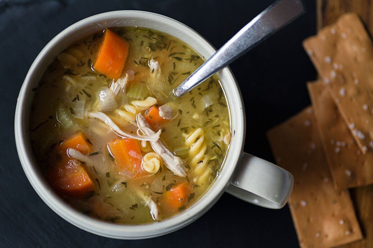 The image of crackers and a cup with soup, carrots, and noodles is perfect for cooking in batches and saving on groceries.