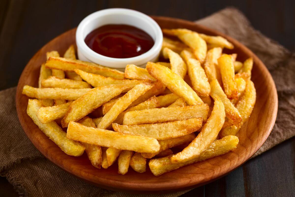 The picture tells about a bowl of french fries with a cup of ketchup which are easy to prepare at home and cost a fraction of what you'd spend eating out. 