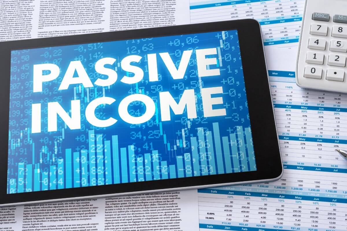 The picture tells about papers with numbers and notes, a calculator, and a tablet with a screen display which means building passive income streams free up time while still contributing to financial growth and independence.