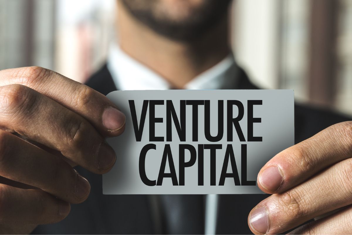 A man's hand holding a paper with venture capital wording.