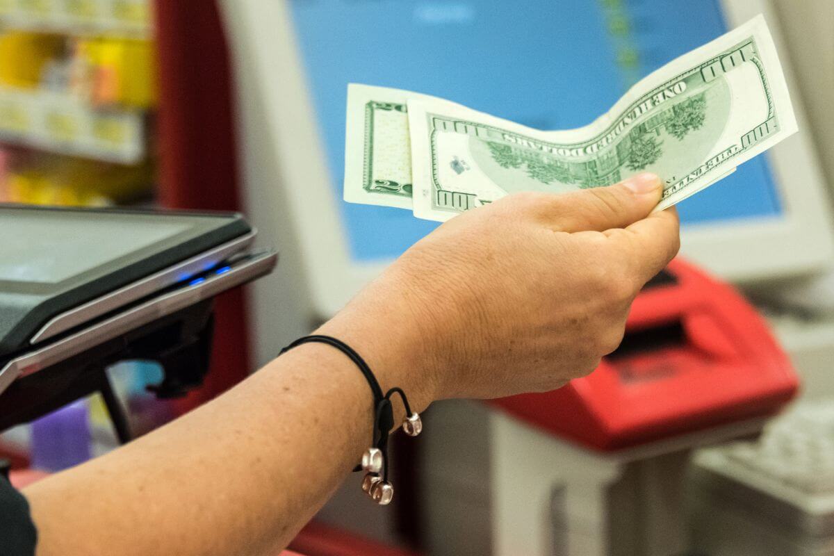 The image tells about a customer's hand paying the cashier in cash which refers to spending mindfully over material items.