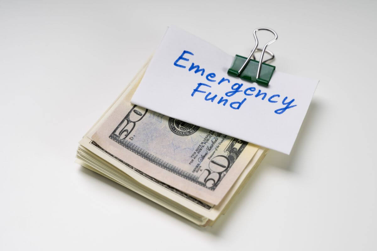 The photo shows folded dollar bills with clip and notes on it indicating to not prioritizing an emergency fund can spiral into financial chaos.