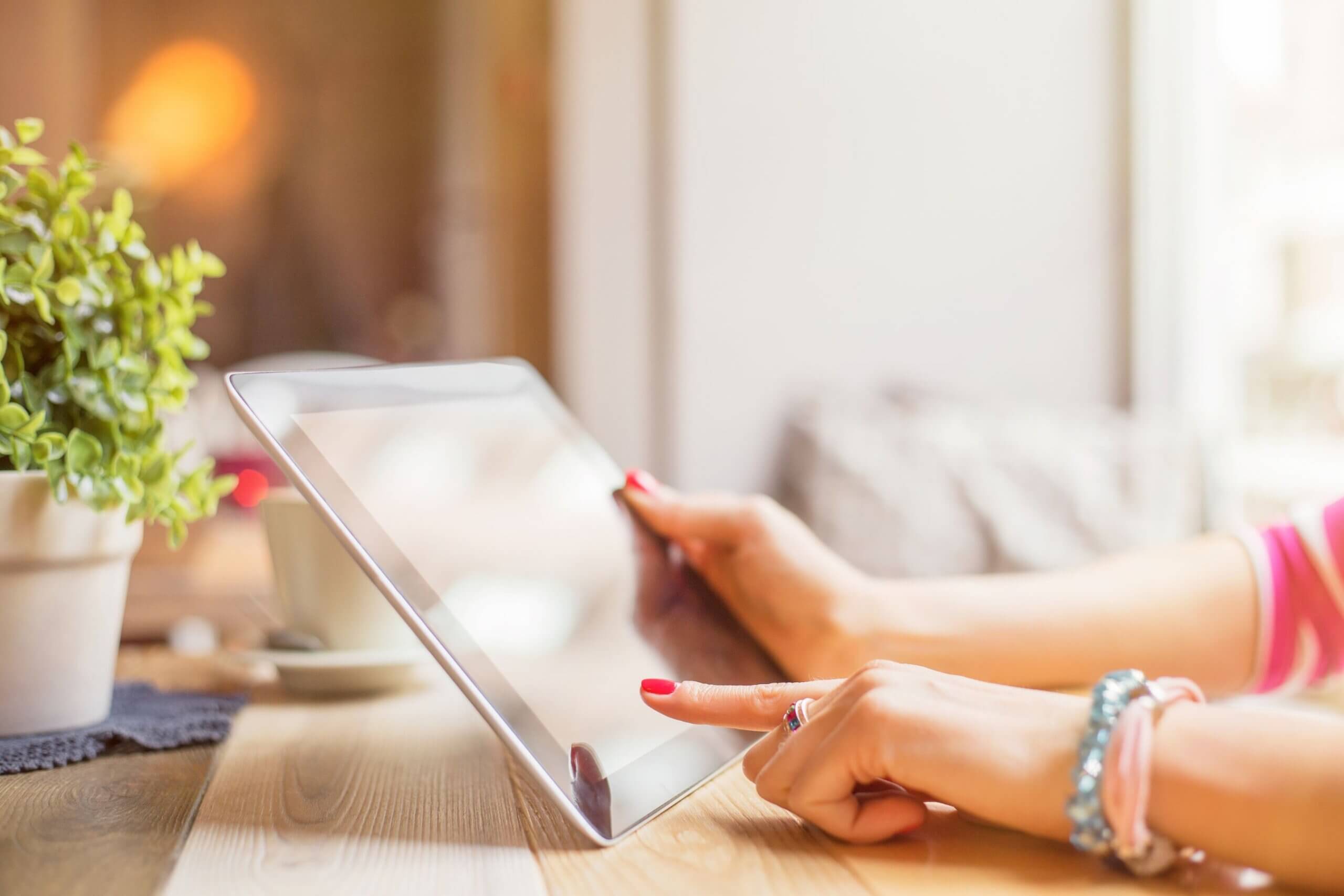 The photo of a girl's hand using a tablet while sitting at the table indicates forgetting to account for subscription services and eating away at your budget without realizing it.