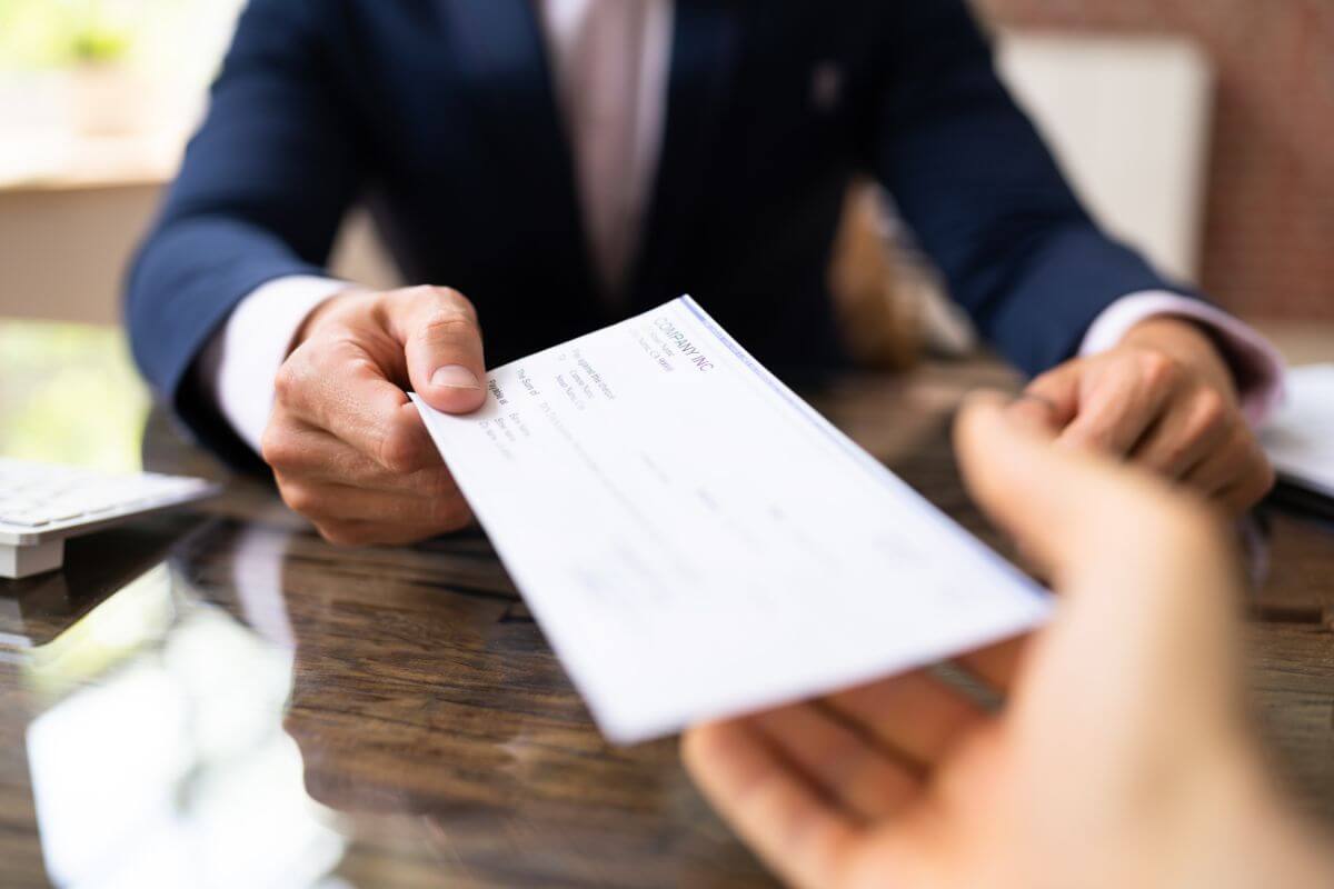 The photo shows a boss giving a piece of paper to his employee which refers to living paycheck to paycheck without a saving buffer could leave you scrambling.