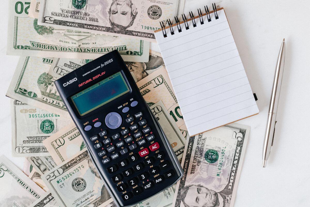 The picture tells about dollar bills, a pen, a mini notebook, and a calculator which means not having clear financial goals can lead to overspending.