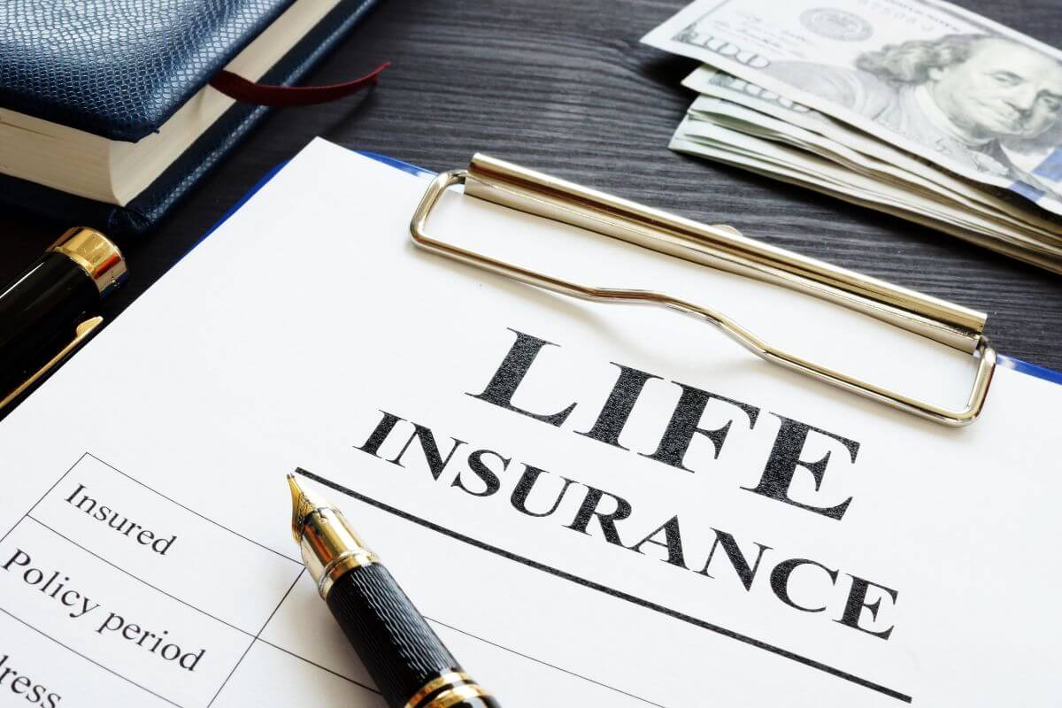 The image tells about dollar bills, a notebook, a pen, and a clipboard with a piece of paper with notes referring to life insurance premiums that might no longer be necessary if you've saved enough and your family is financially independent.