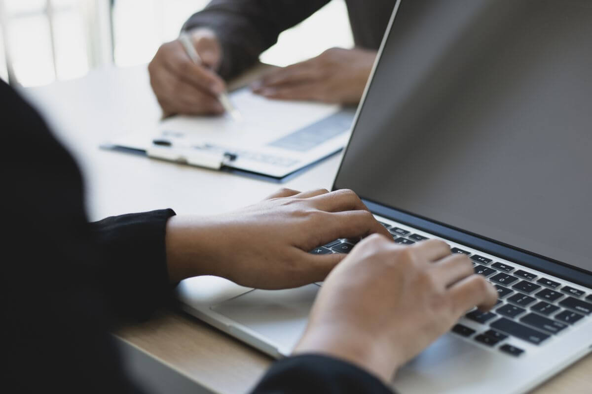 The photo of an employer using a laptop and an employee writing on the paper referring to taking advantage of employer 401(K) matching contributions to earn full match boosts your savings without extra effort.