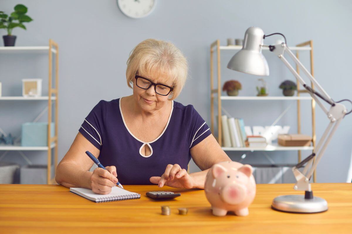 The photo tells about a lamp, a piggy bank, coins, and a senior calculating while writing in the notebook which means to reduce unnecessary expenses and redirect the money into savings to grow your money over time.
