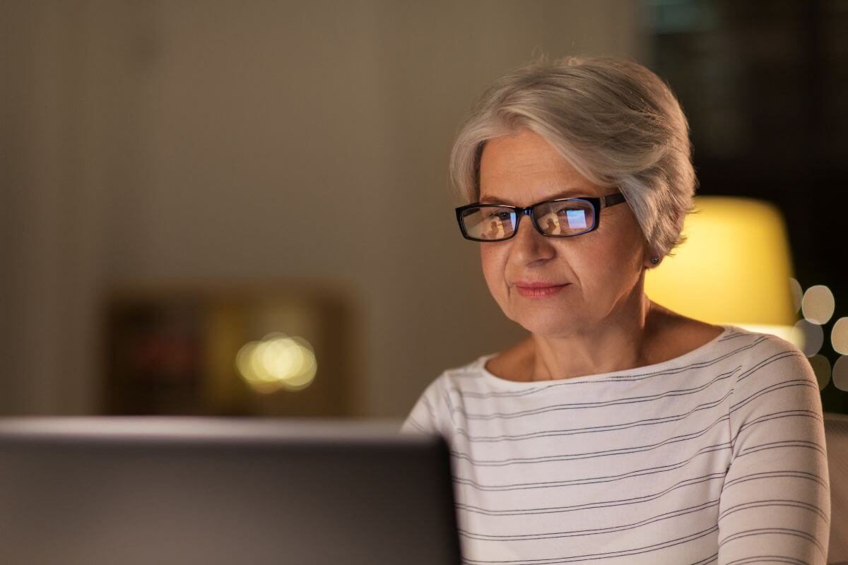 The picture shows a senior using a laptop to find a side hustle job that can provide extra income to grow your retirement fund.