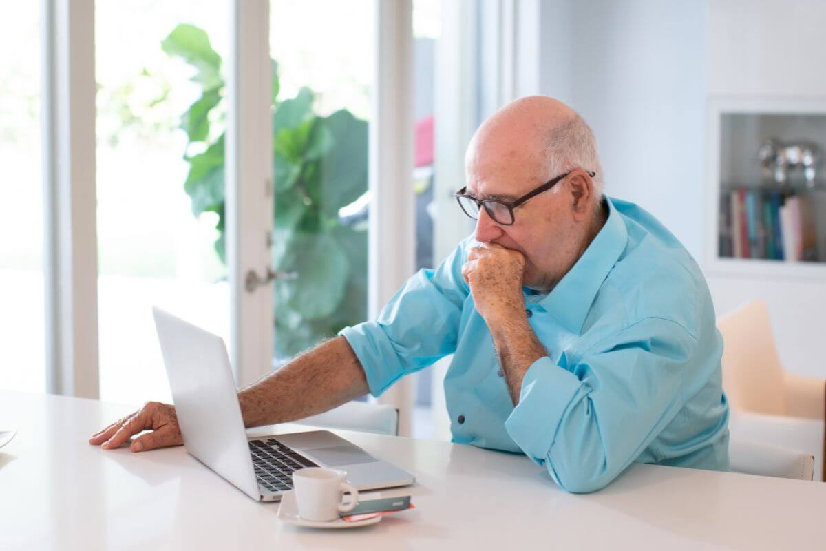 The photo tells about a coffee on the table and a senior looking at a laptop and wondering what it means to learn what happens if you don't save for retirement, starting now helps you avoid these challenges and build a secure future.