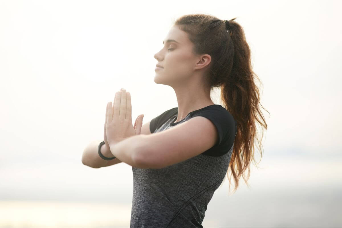 The photo of a girl praising both hands relaxing referring to reinforcing a mindset of abundance instead of scarcity helps make better choices and attract more wealth into your life.
