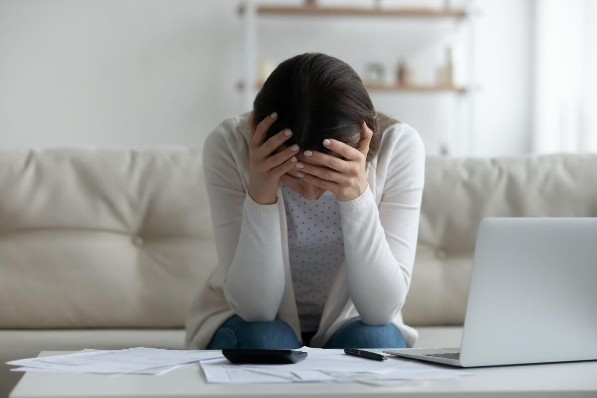 The photo shows a laptop, papers on the table, and a girl frustrated which means bad debt can lead to financial stress making it harder to reach financial independence.