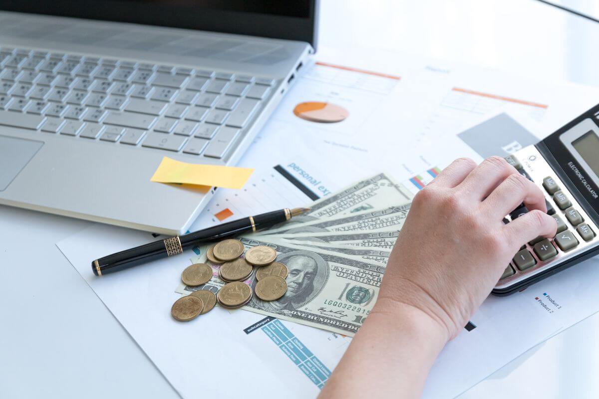 The picture shows a laptop, a pen, coins, dollar bills, papers, and a girl's hand calculating which means to use good debt only when it aligns with your financial goals and offers a clear return.