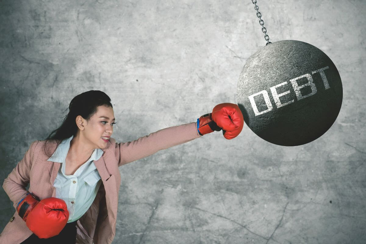 The image shows a girl wearing gloves and punching the wrecking ball with a note which means to get rid of bad debt now to a more stable and stress-free financial future.