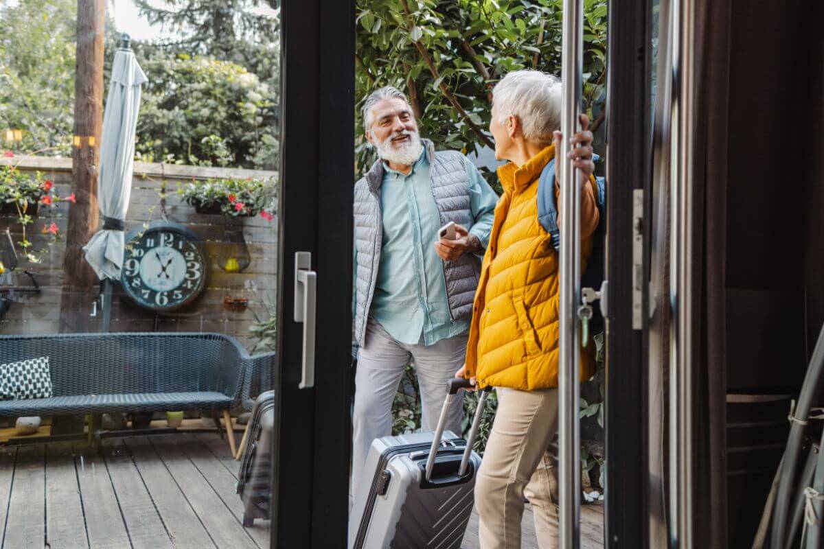 The picture tells about the seniors carrying their luggage while entering their lodging place which means senior discounts on travel and lodging can make vacations more affordable.