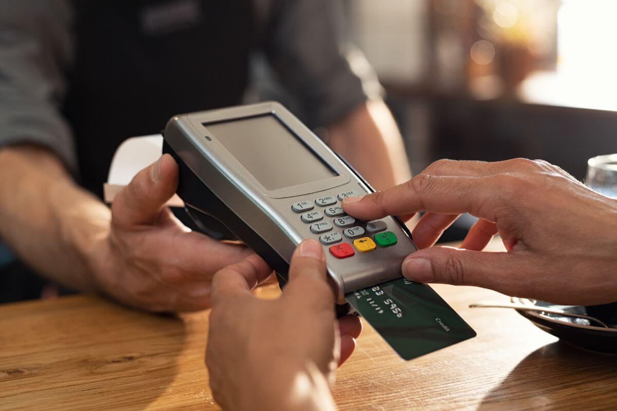 The picture shows a cashier's hand giving the swiping card to the customer to insert his card into it and typing the pin code indicating to stop treating your credit card like free money that comes with interest and fees that add up fast.