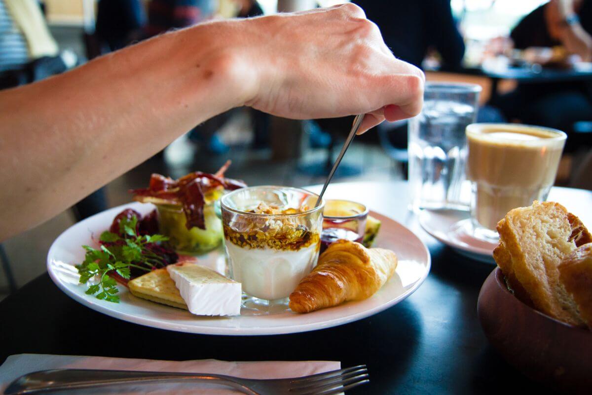 The picture tells about coffee, water, and a man's hand eating the food on a plate which refers to not eating out five nights a week, and cooking at home saves money and helps you cover essentials. 