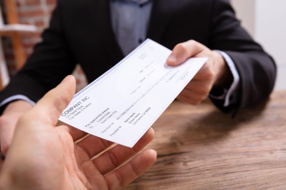 The image shows a boss's hand giving a piece of paper to his worker's hand which means that big-ticket purchases can wait if you're living paycheck to paycheck and prioritizing your needs over wants to work toward financial stability.