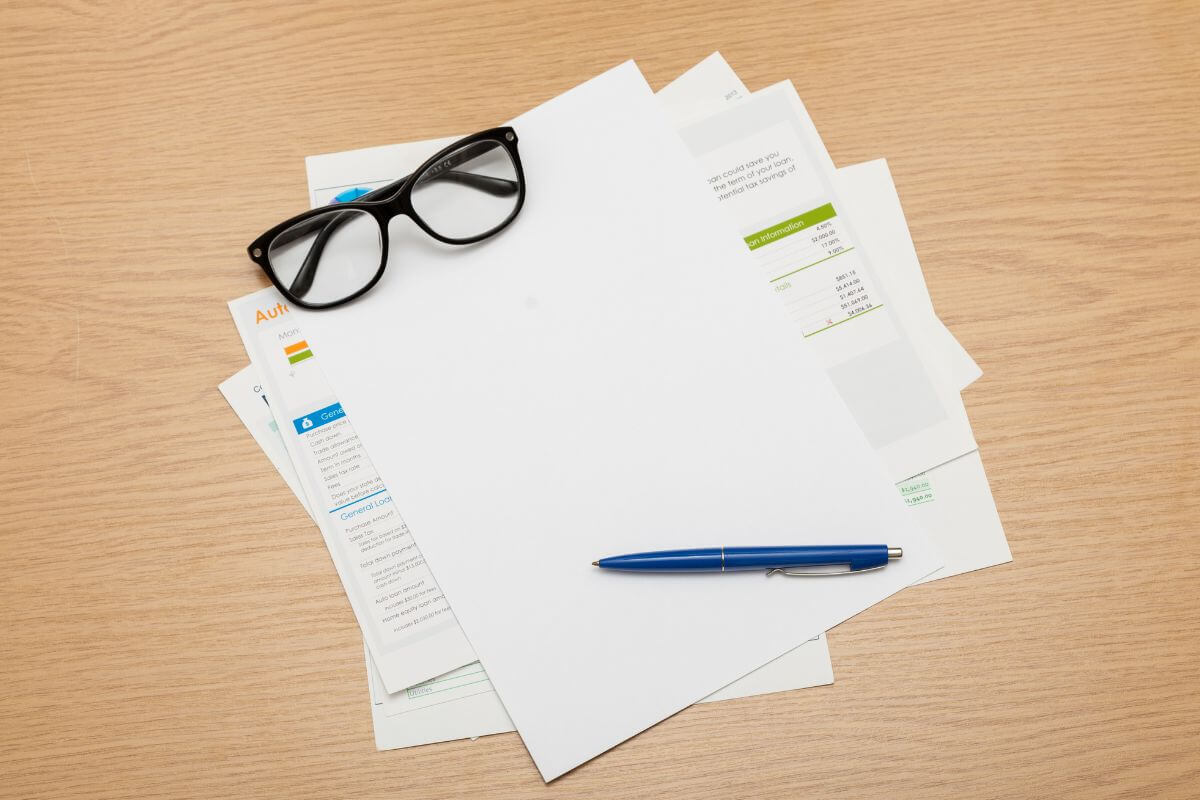 The image shows papers, a pen, and an eyeglass, referring to gathering important financial documents in a fireproof folder to help access funds after an emergency.