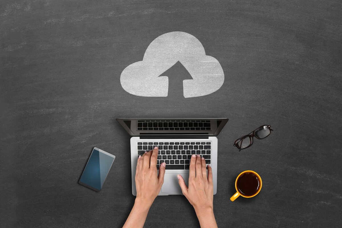 The photo shows a coffee, a phone, an eyeglass, an upload icon, and a girl's hand tying on a laptop indicating that creating a digital backup ensures that even if physical documents are lost, you can still access everything you need.