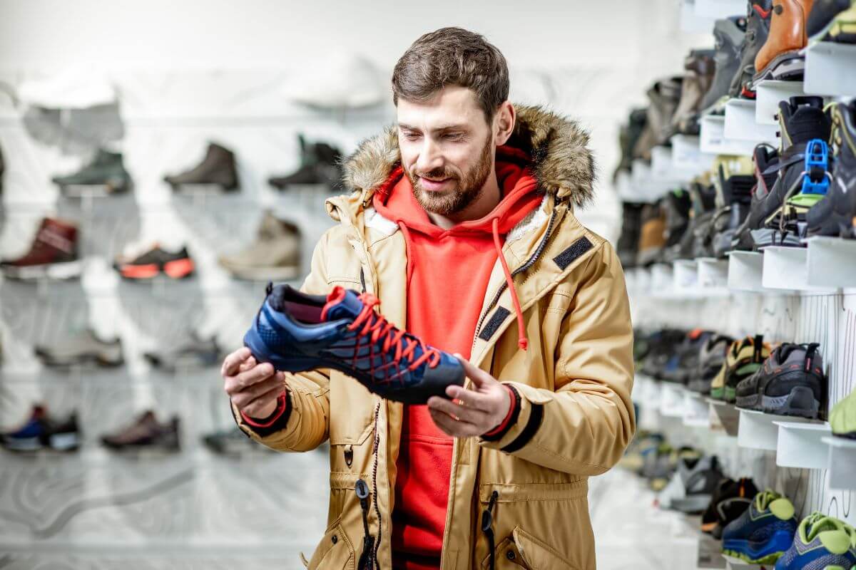 The picture shows a man picking a shoe in a store indicating to focus on quality over quantity for durable purchases which is a smart way to spend less and love better.