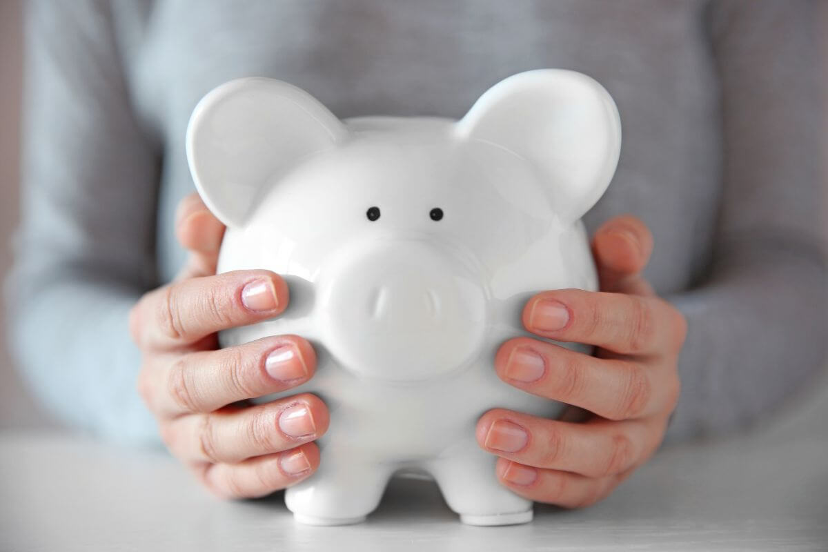 The picture shows a girl's hand holding a piggy bank referring to more frugal living tips to help you save money, reduce waste, and focus on what truly matters. 
