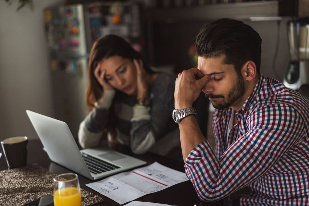 The photo tells about a couple looking at the papers and a laptop with frustrations indicating that leaving debts unresolved can haunt your family after you're gone.