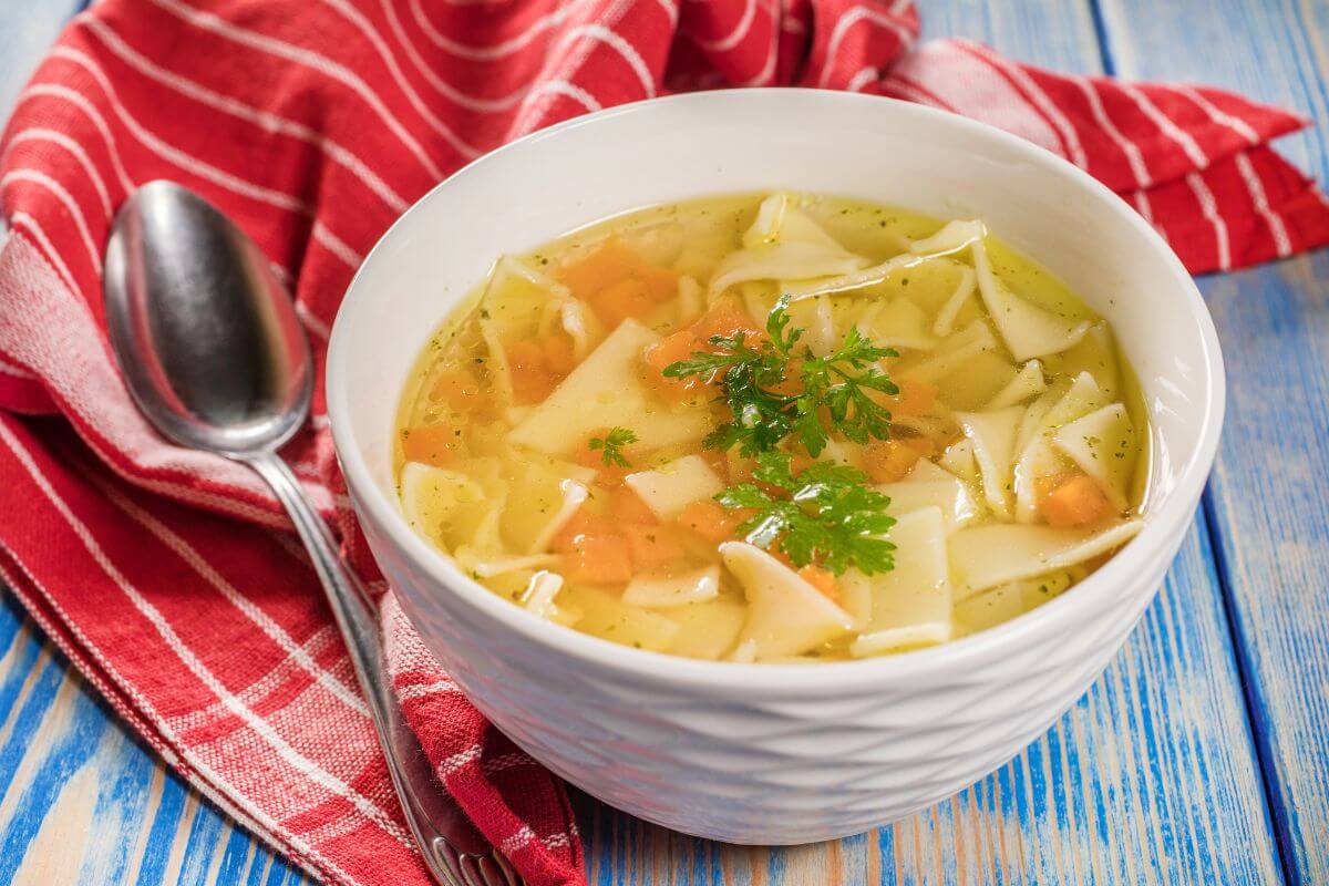 The photo of a fabric, a spoon, and a bowl of store-bought broth which is more expensive than making your own from leftover vegetables and meat scraps saves money and reduces waste.
