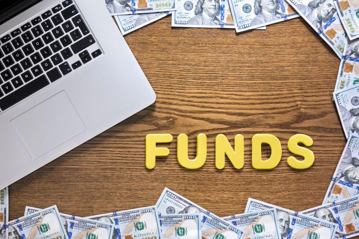 The picture tells about a laptop, dollar bills,  and letters on the table indicating to look for funds that focus on sustainability and ethics to help build a portfolio that's both profitable and responsible.