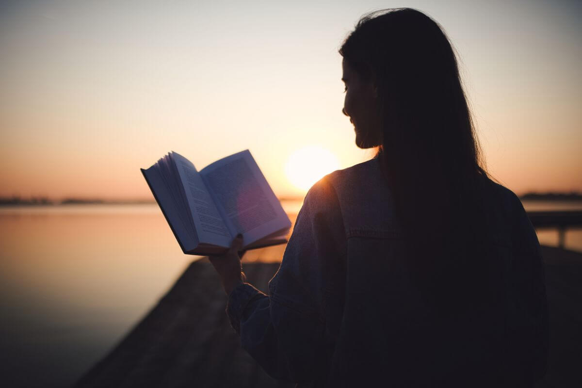 The image tells about a girl reading a book beside the sea titled Your Money or Your Life by Vicki Robin and Joe Dominguez, this classic book helps you rethink how you spend and save money by focusing on what truly matters.