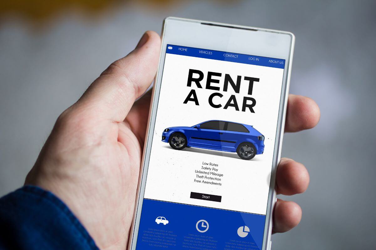 The image shows a man's hand holding a phone with a screen display which means that renting a car without a credit card is possible but may require a deposit or extra paper. 