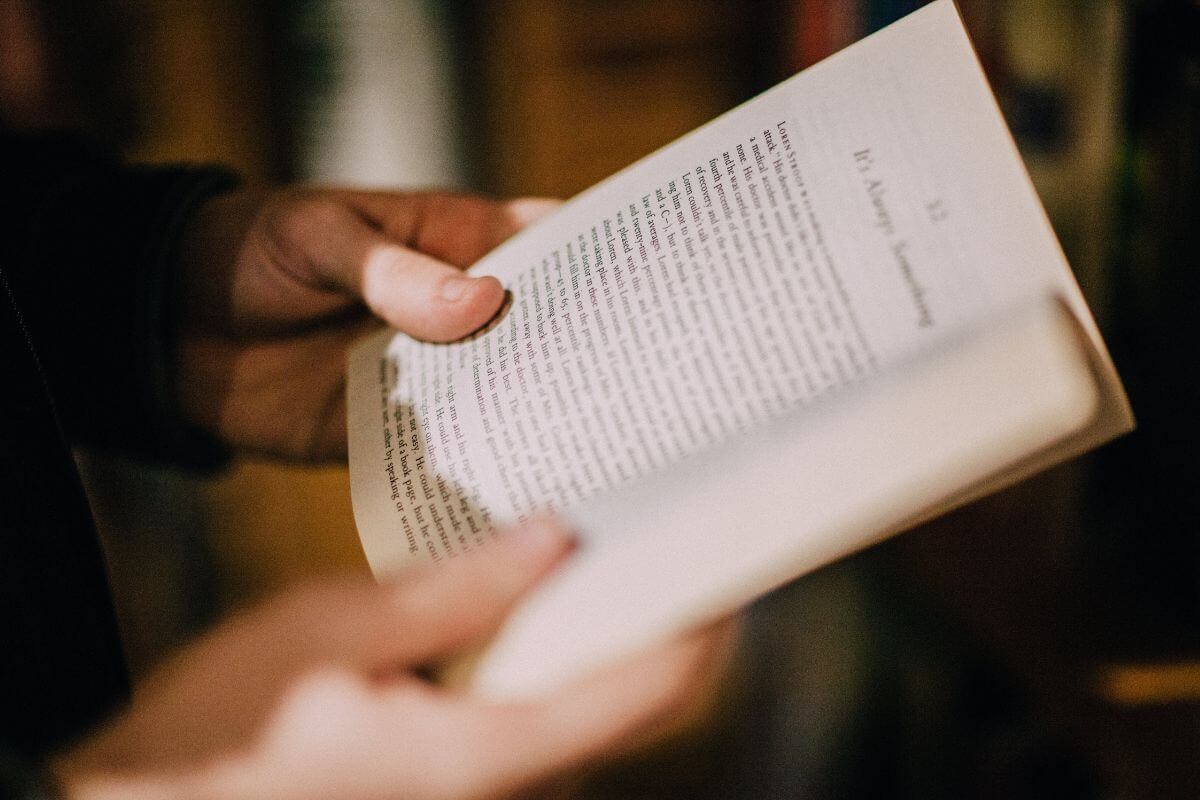 The picture shows a girl's hand holding and reading a book titled The Psychology of Money by Morgan Housel which explains how emotions and habits affect financial decisions.