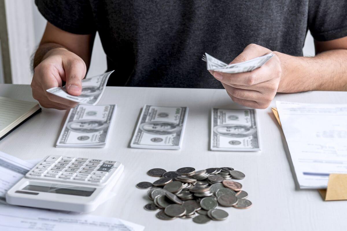 The photo of papers on the table, coins, a calculator, and a man grouping the dollar bills which means ways to develop better budgeting habits to avoid needing credit cards helps you live within your means and handle your money smarter.