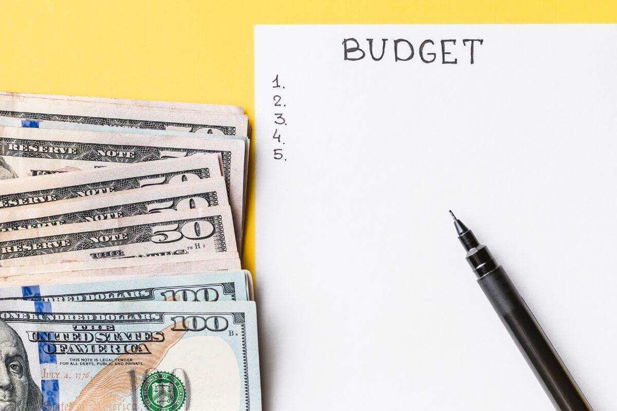 The image of dollar bills, a pen, and a piece of paper with notes indicating to get your budget in shape to help you avoid relying on credit cards and live within your means.