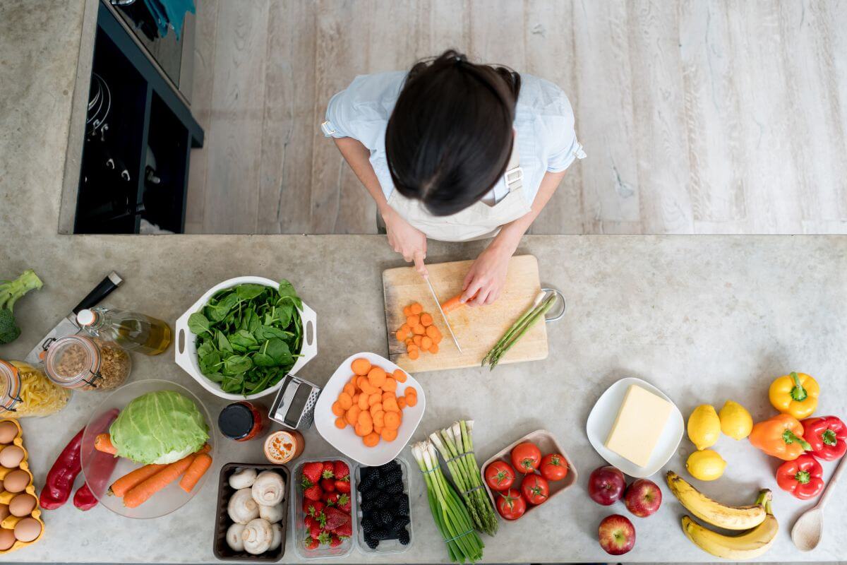 The photo tells about the ingredients needed to be prepared on the table and a girl slicing them which means cooking at home instead of eating out gives you control over portions and ingredients and is more budget-friendly.