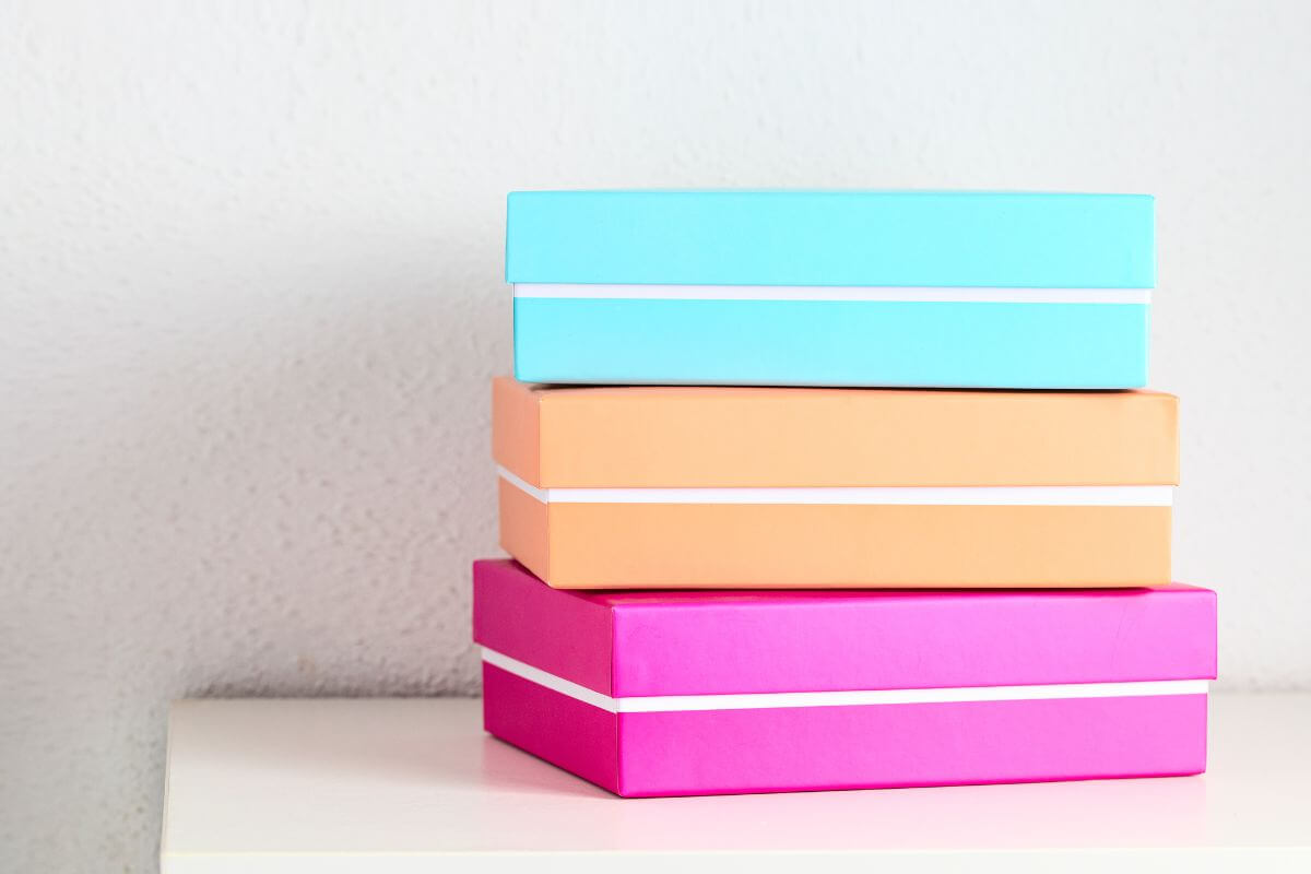 The image tells about the colorful piled boxes on the table referring to unused subscription boxes as a waste of space and money, cancel them to simplify your life and free up funds for what truly matters.  