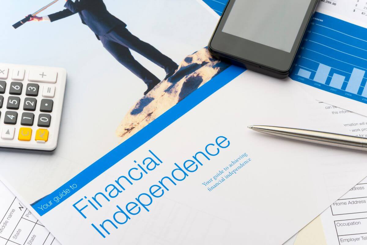 The image shows a calculator, a phone, papers with graphs and notes, a pen, and a magazine with pictures and notes indicating that working with clients who prioritize financial independence can help you focus on achieving your goals instead of accumulating debt or unnecessary investments.