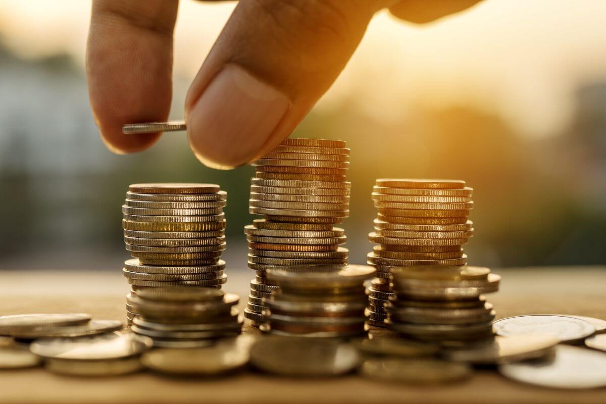 The image tells about coin stocks and a man's hand dropping a coin to it referring to which saving should prioritize first, balancing priorities can help you stay prepared for both long and short-term needs.