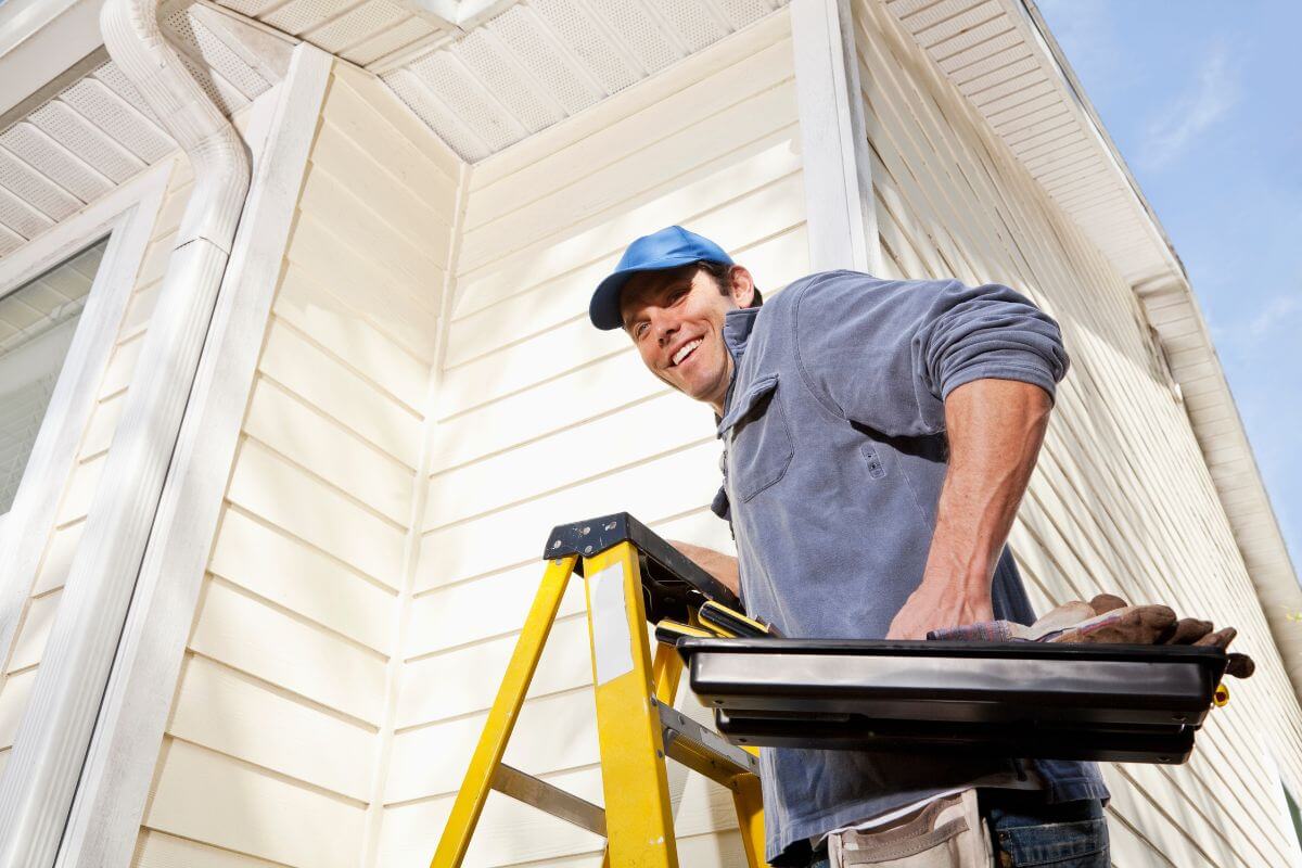 The image shows a man stepping onto the ladder while holding tools in a box indicating to learn to barter services to save money and help everyone stretch their resources further.