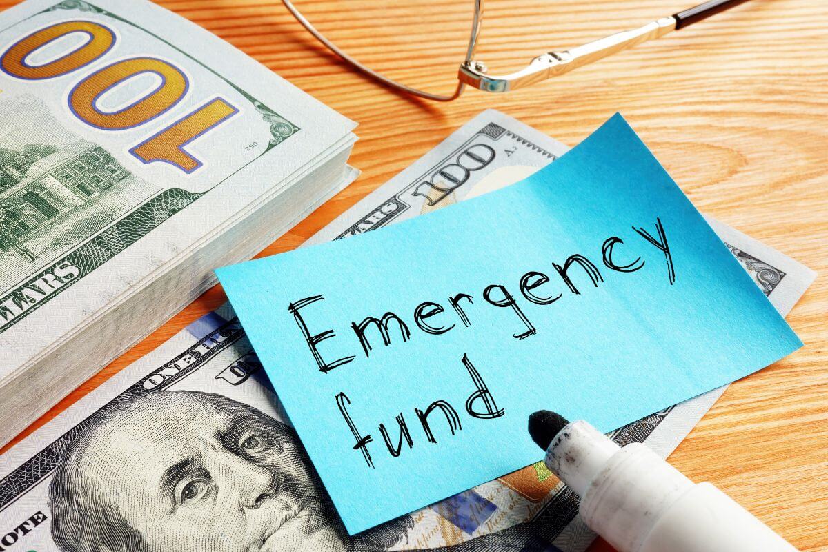 The photo of an eyeglass, dollar bills, a marker, and a piece of paper with notes referring to how much one should have in an emergency fund versus other savings, both ensure financial security for any situation.