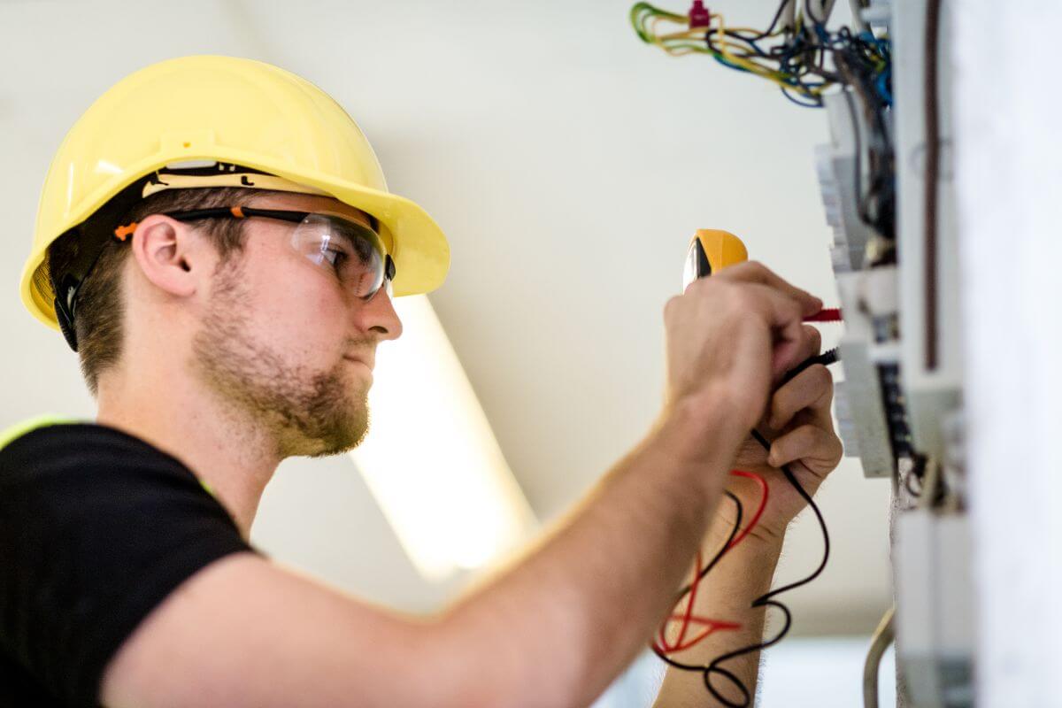 The image shows an Electrician with a safety helmet fixing the wires which earn good pay by keeping homes and businesses running smoothly.