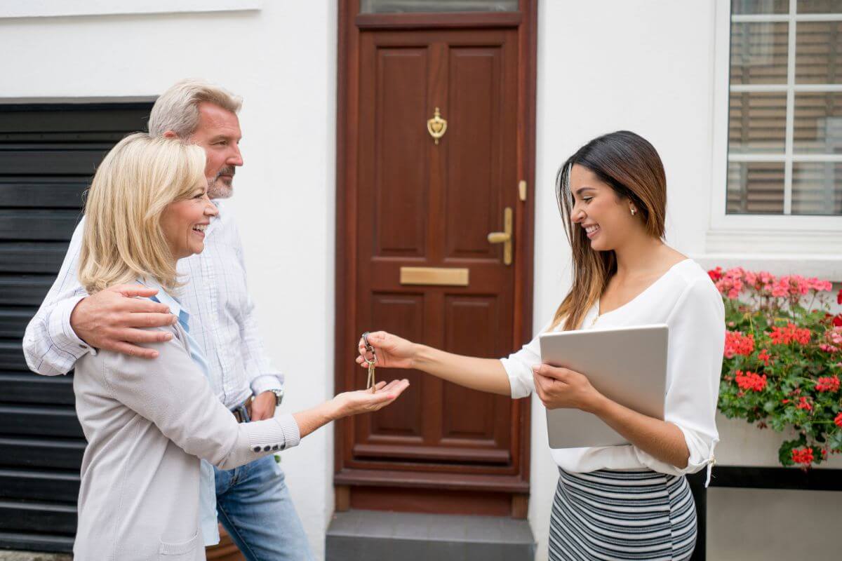 The photo of a couple and a girl giving the key to them while holding a paper in front of a house refers to real estate agents earning top dollar by helping clients buy and sell homes.