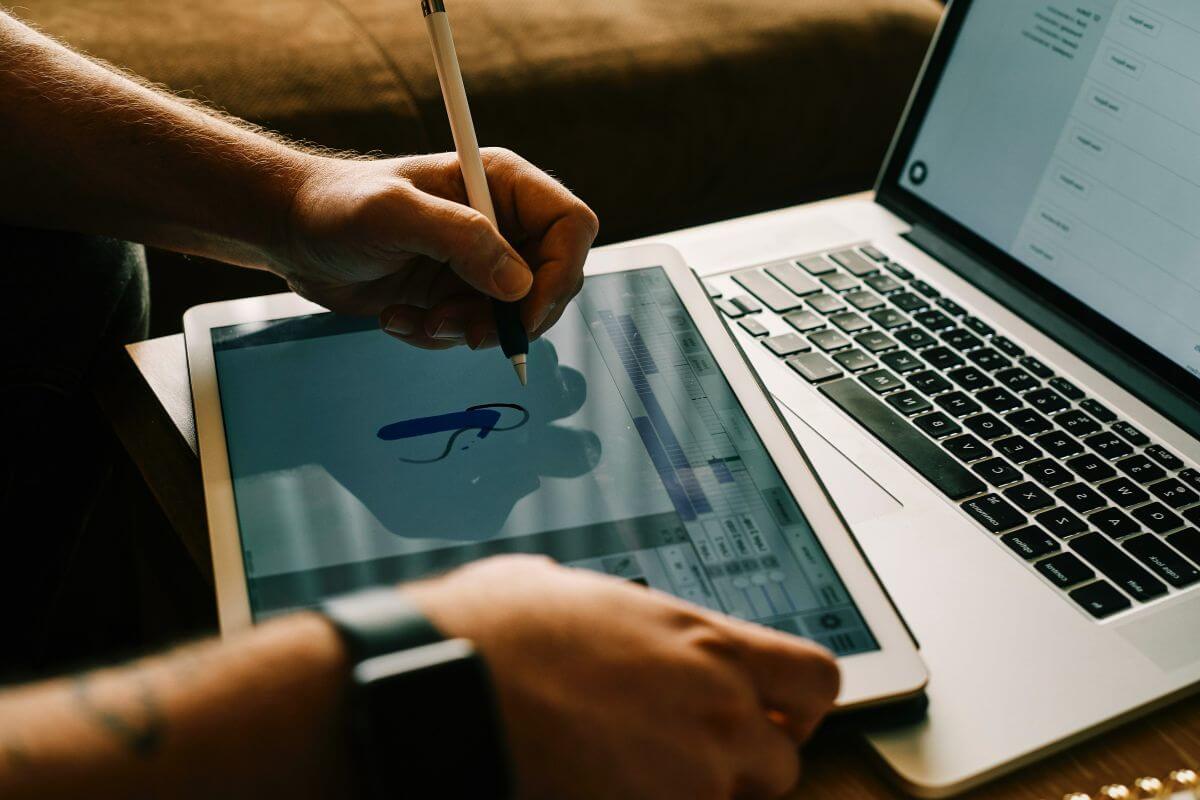 The photo tells about a laptop and a man's hand drawing on a tablet device referring to a freelance graphic designer as a flexible career where creativity meets good pay.