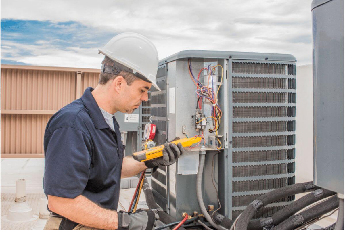 The image shows a man fixing a wire of a machine using a tool with his safety helmet indicating that the HVAC Technician keeps the heating and cooling system running effectively, which they can earn $50 an hour.