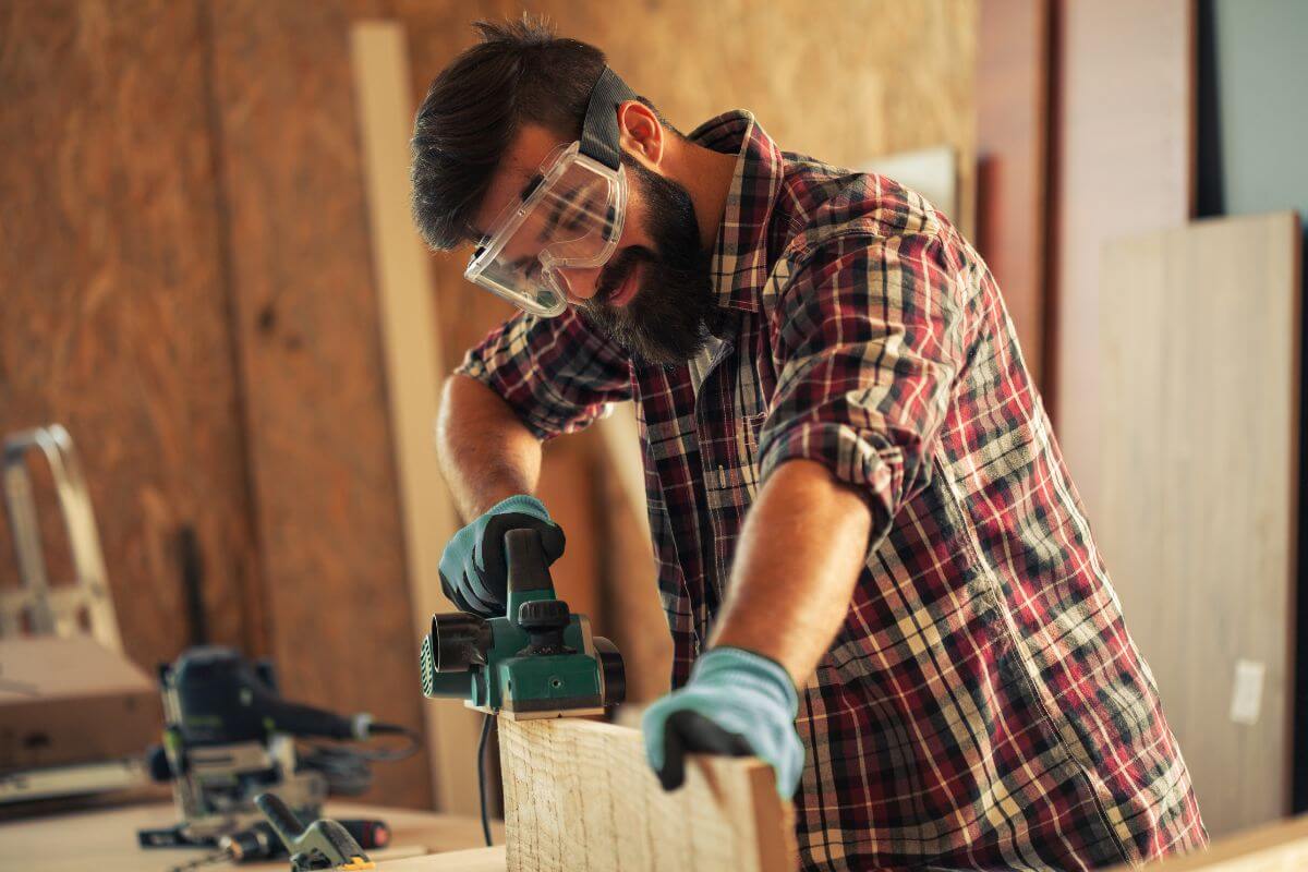 The photo tells about a carpenter using a safety goggle while smoothing the wood using a machine that brings designs to life while earning over $50 an hour.